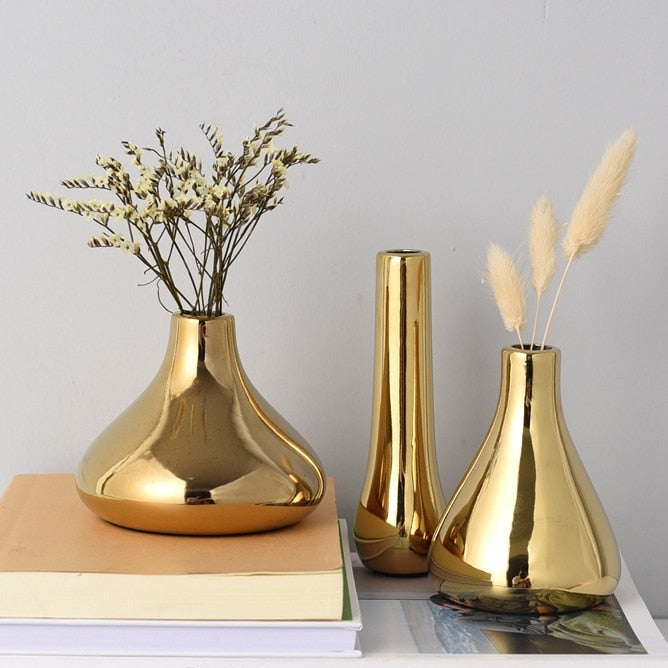 Three small gold vases on books with flowers