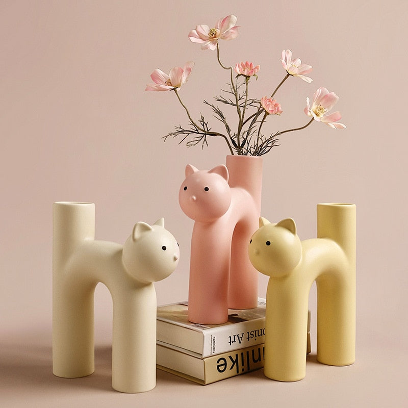 Three cat vases in cream, pink and yellow with flowers and books