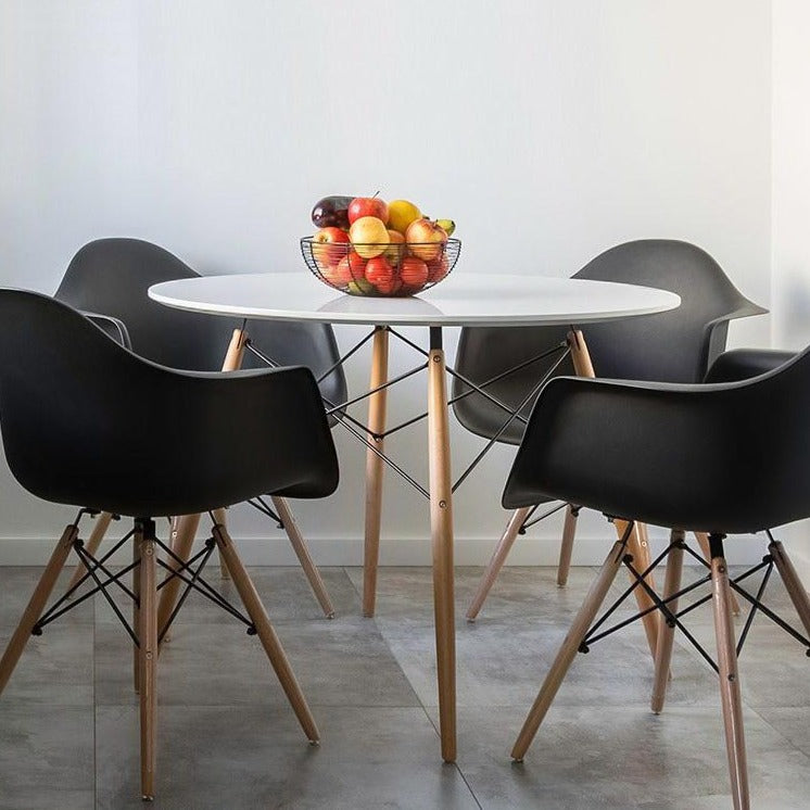 White 4 seater dining table with solid beech wood legs shown with black dining chairs and bowl of fruit