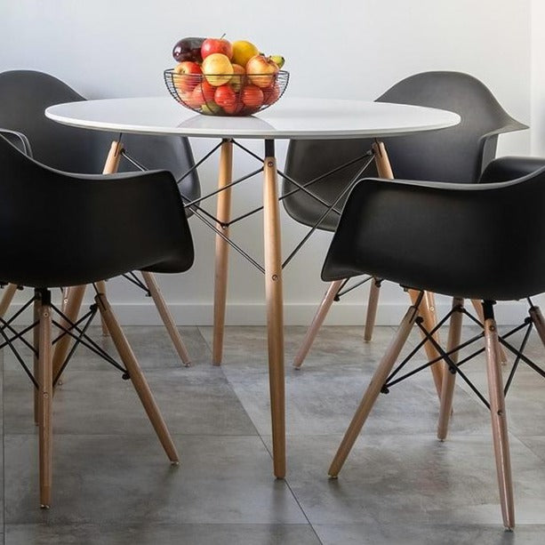 White 4 seater dining table with solid beech wood legs show with black chairs and bowl of fruit