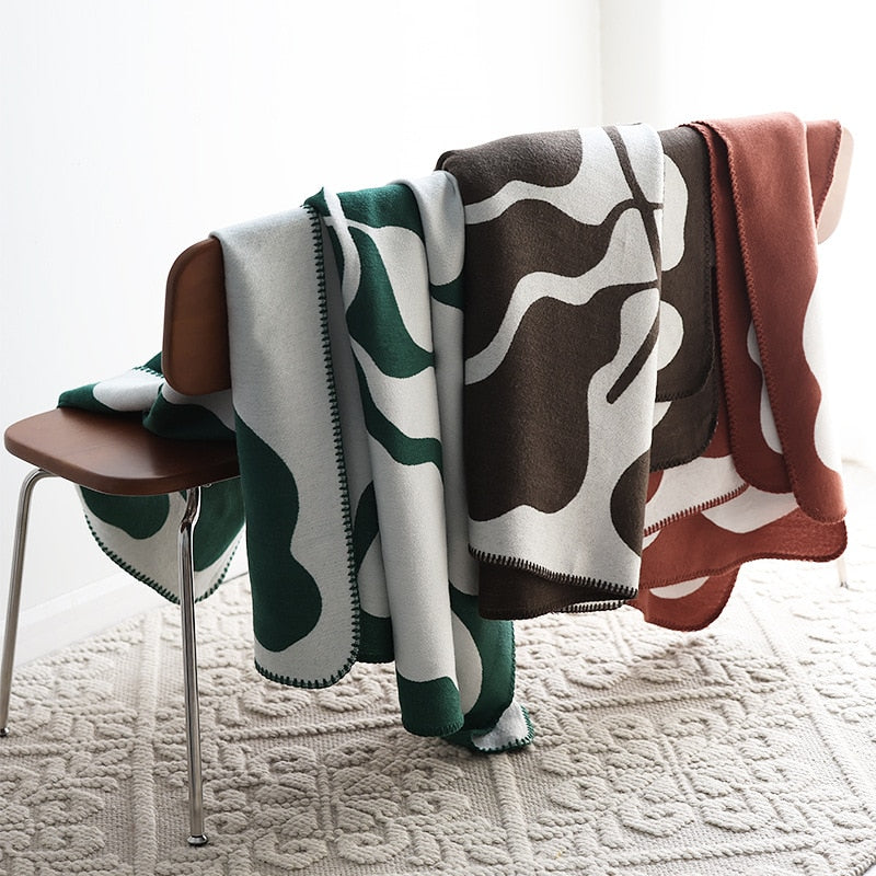 Three knitted blankets with bold pattern over chair with stitched edges