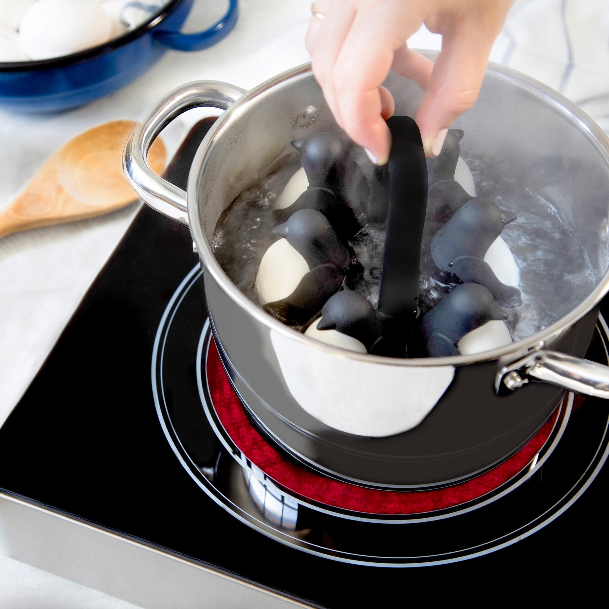 Person holding handle of penguin shaped egg holder while it sits in boiling pot of water