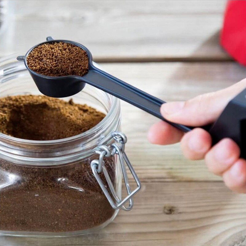 Person holding giraffe coffee scoop with coffee over jar of coffee