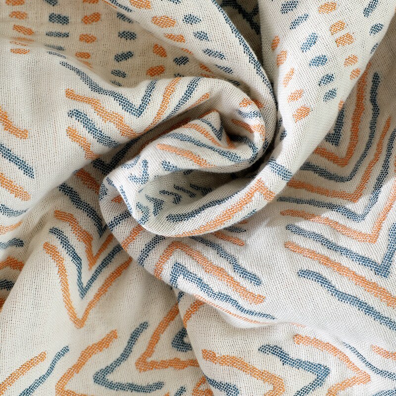 Close up of cream throw blanket with abstract pattern of earthy blues and orange