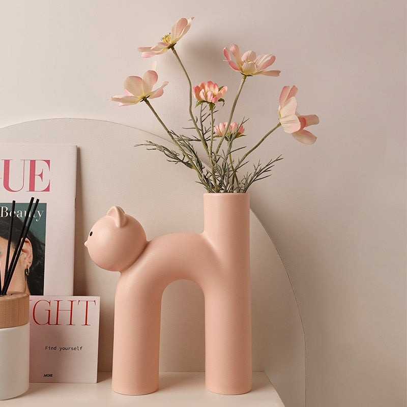 Pink cat vase on shelf with books and flowers