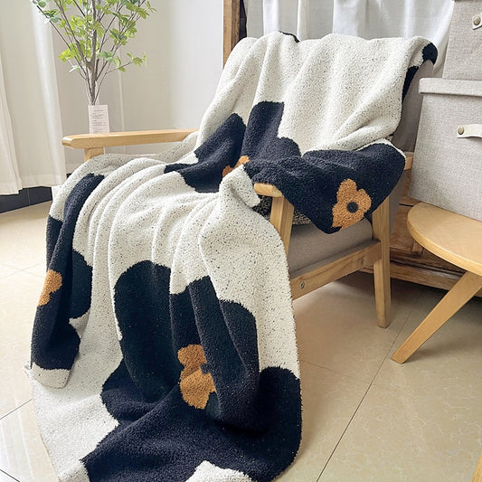 Soft knitted blanket on chair with large black and amber flowers