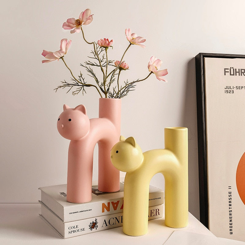 Pink and yellow cat vases on shelf with flowers and books