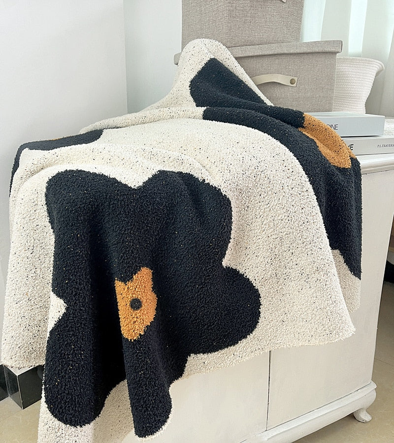 Soft knitted blanket on shelf with large black and amber flowers